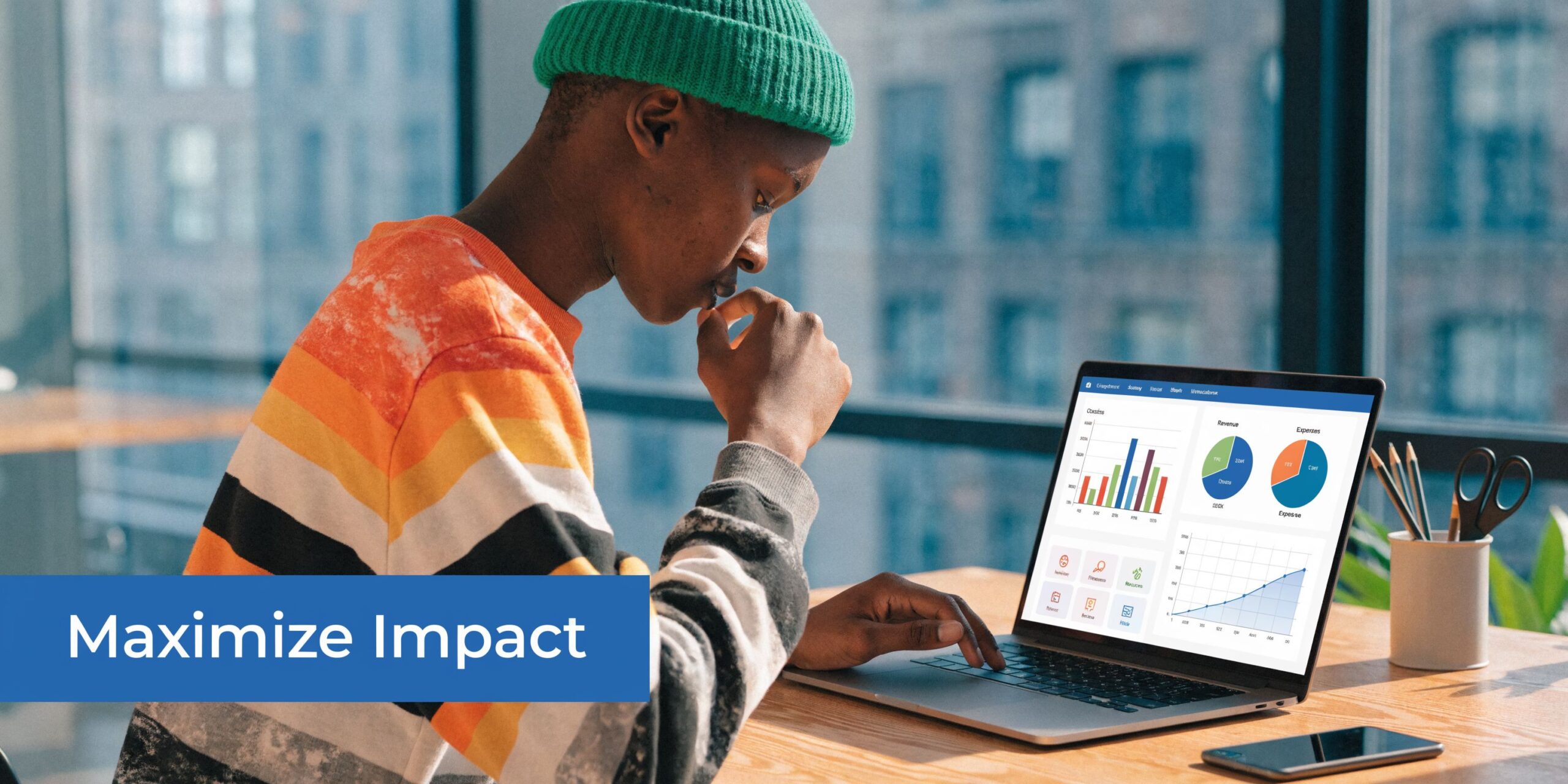 A young person wearing a green beanie works on a laptop showing data charts in an office.