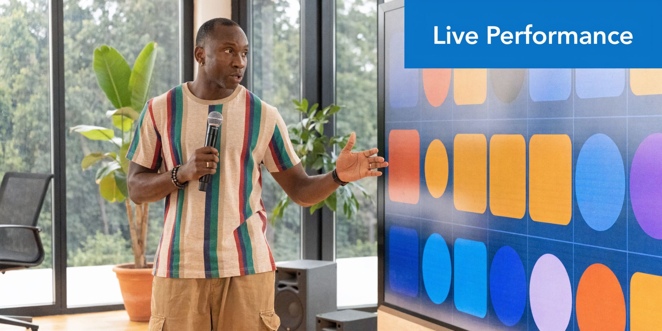 A man in a striped shirt stands in front of a screen while hosting a webinar presentation.