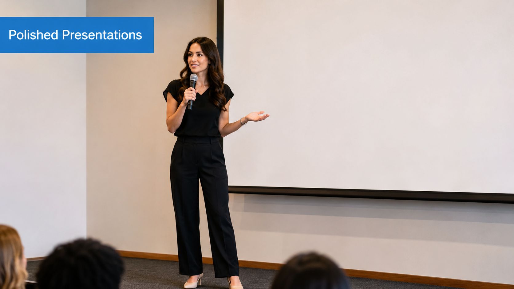 A professional woman speaking into a microphone while standing in front of a projection screen.